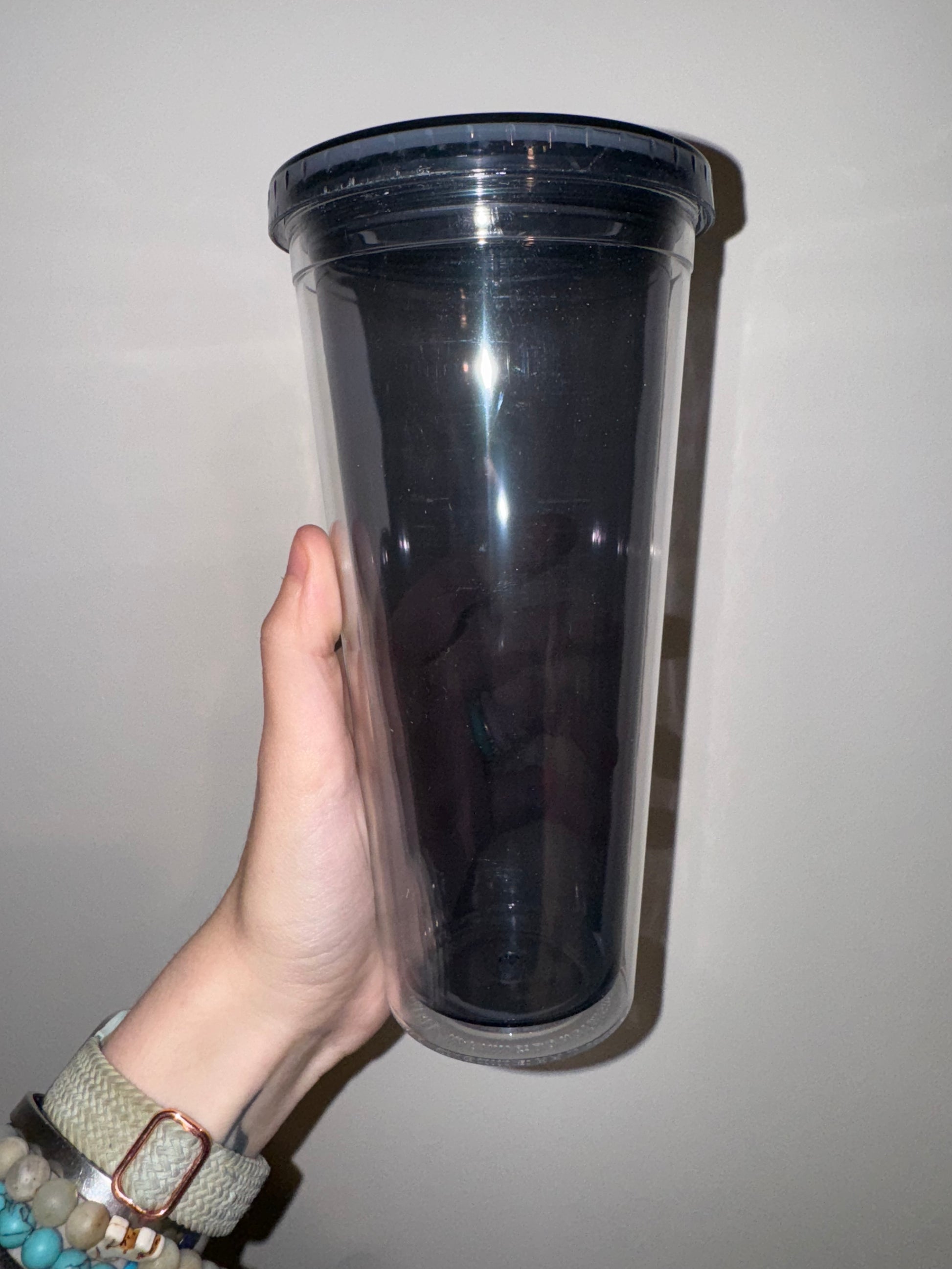 Black acrylic container held by a hand against a plain background