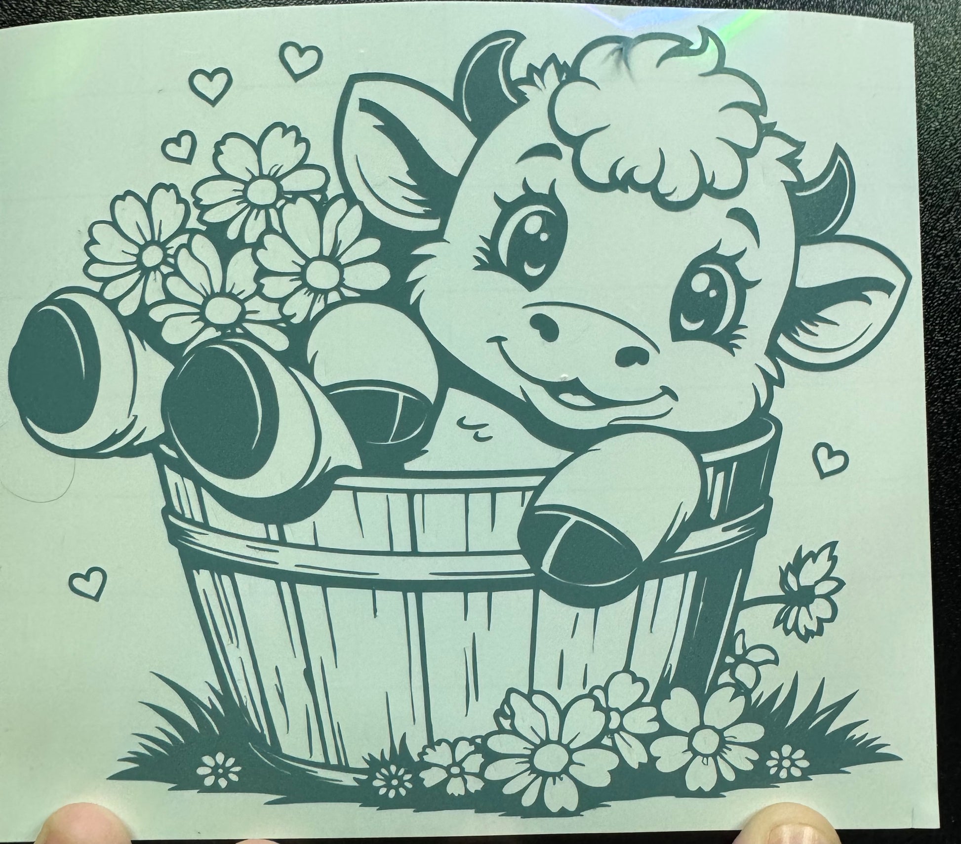 A decorative sticker depicting a cartoon cow in a bucket with flowers and hearts around it.