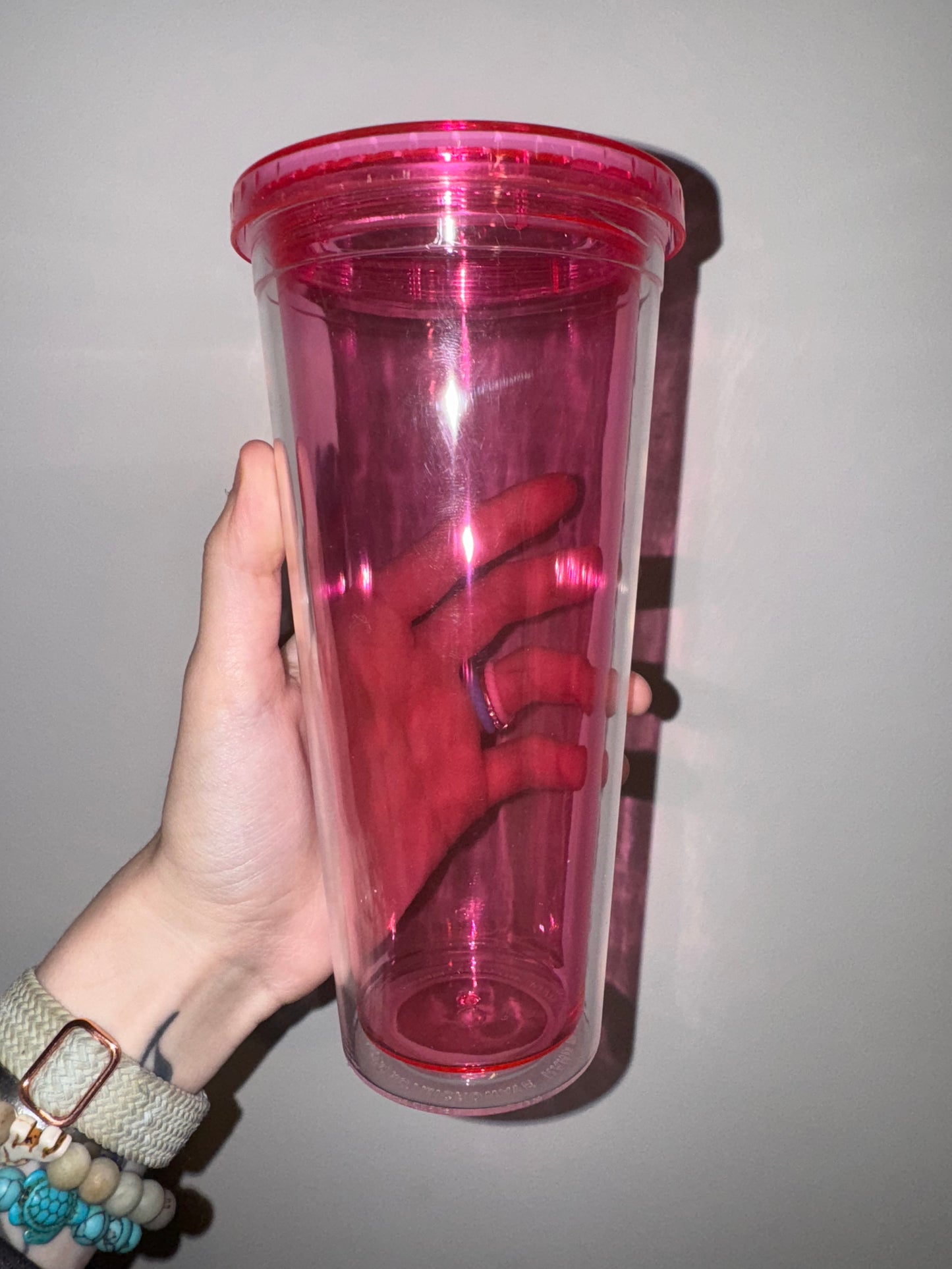 Hand holding a hot pink cylindrical container against a plain background