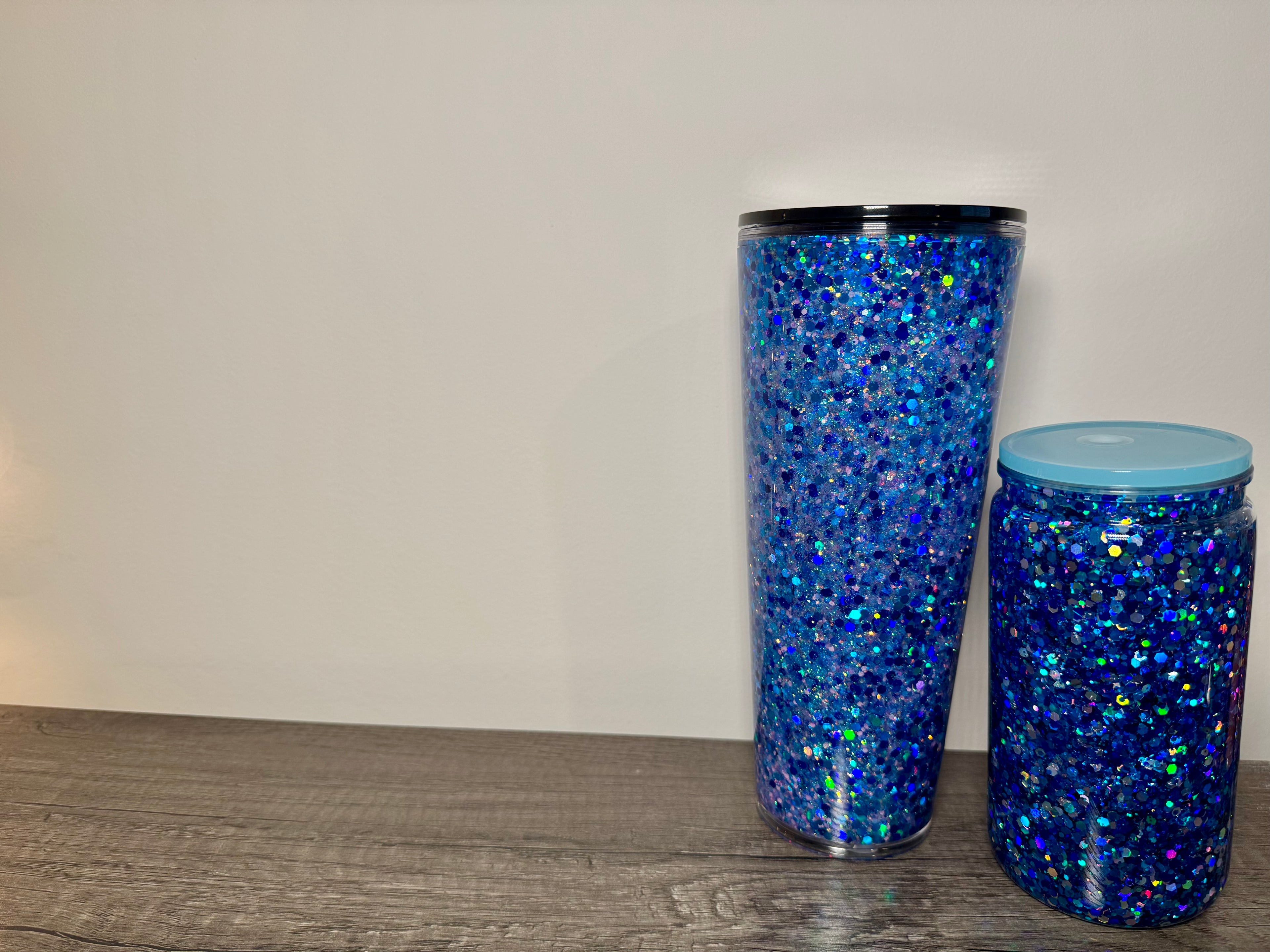 Two blue glittery tumblers on a wooden surface with a neutral background