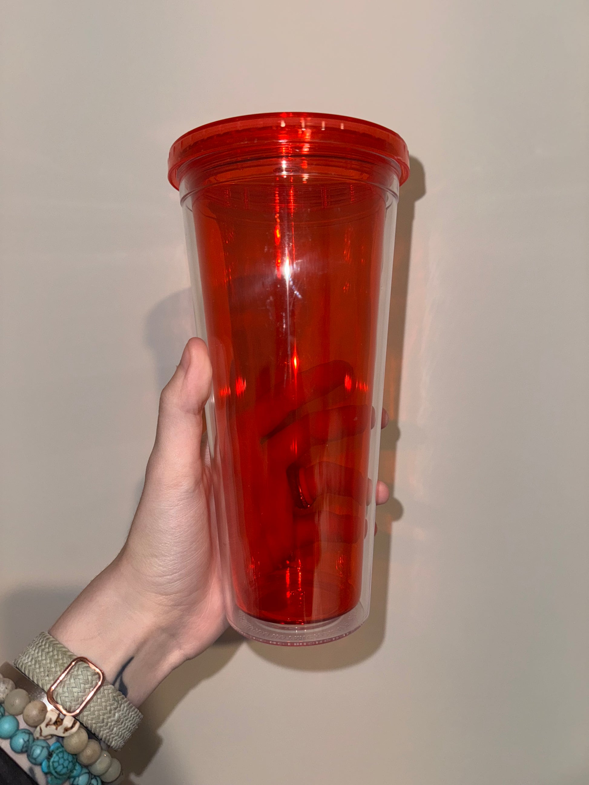 Hand holding a red cylindrical container against a plain background