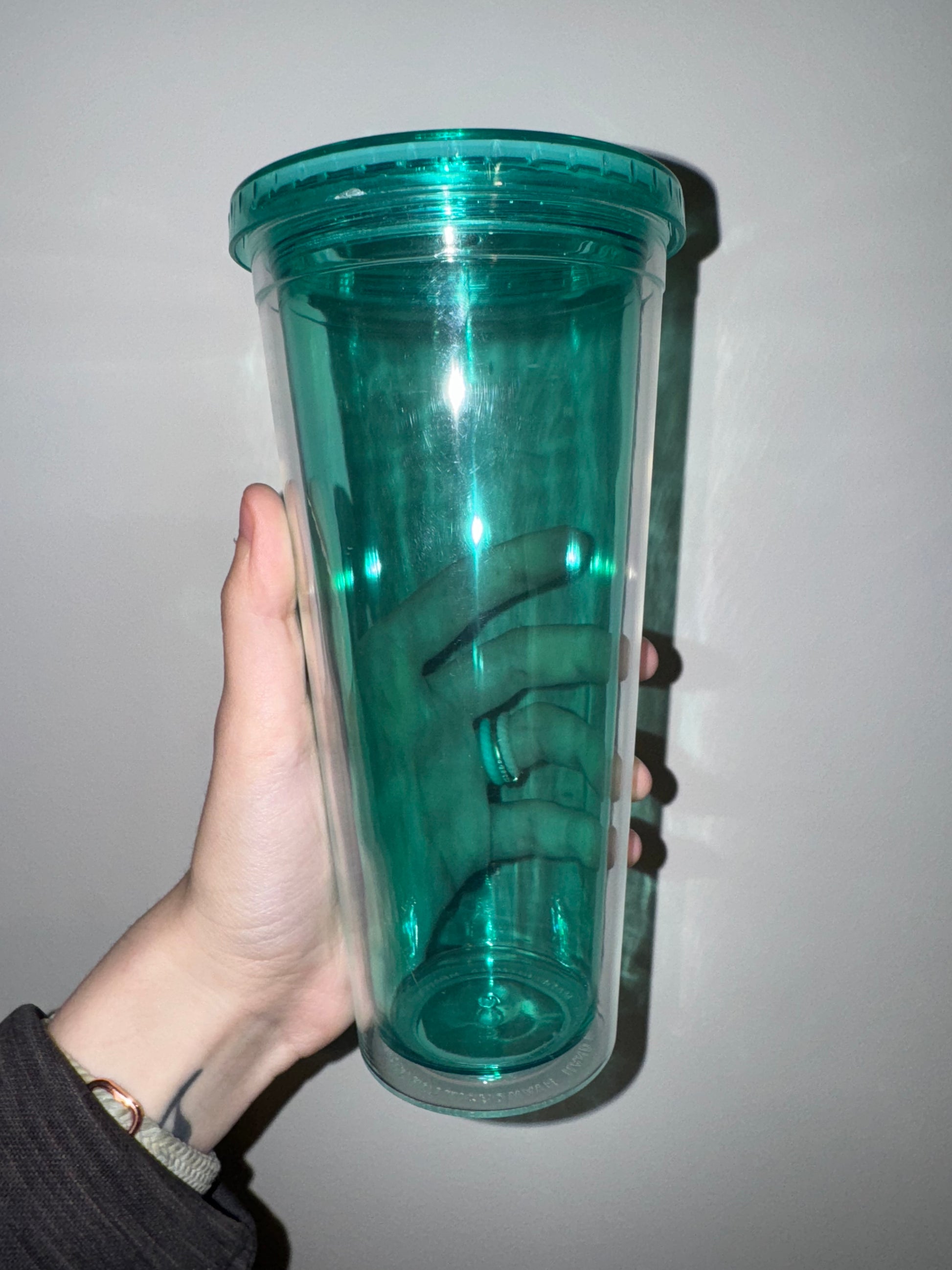 Hand holding a teal tumbler against a plain background