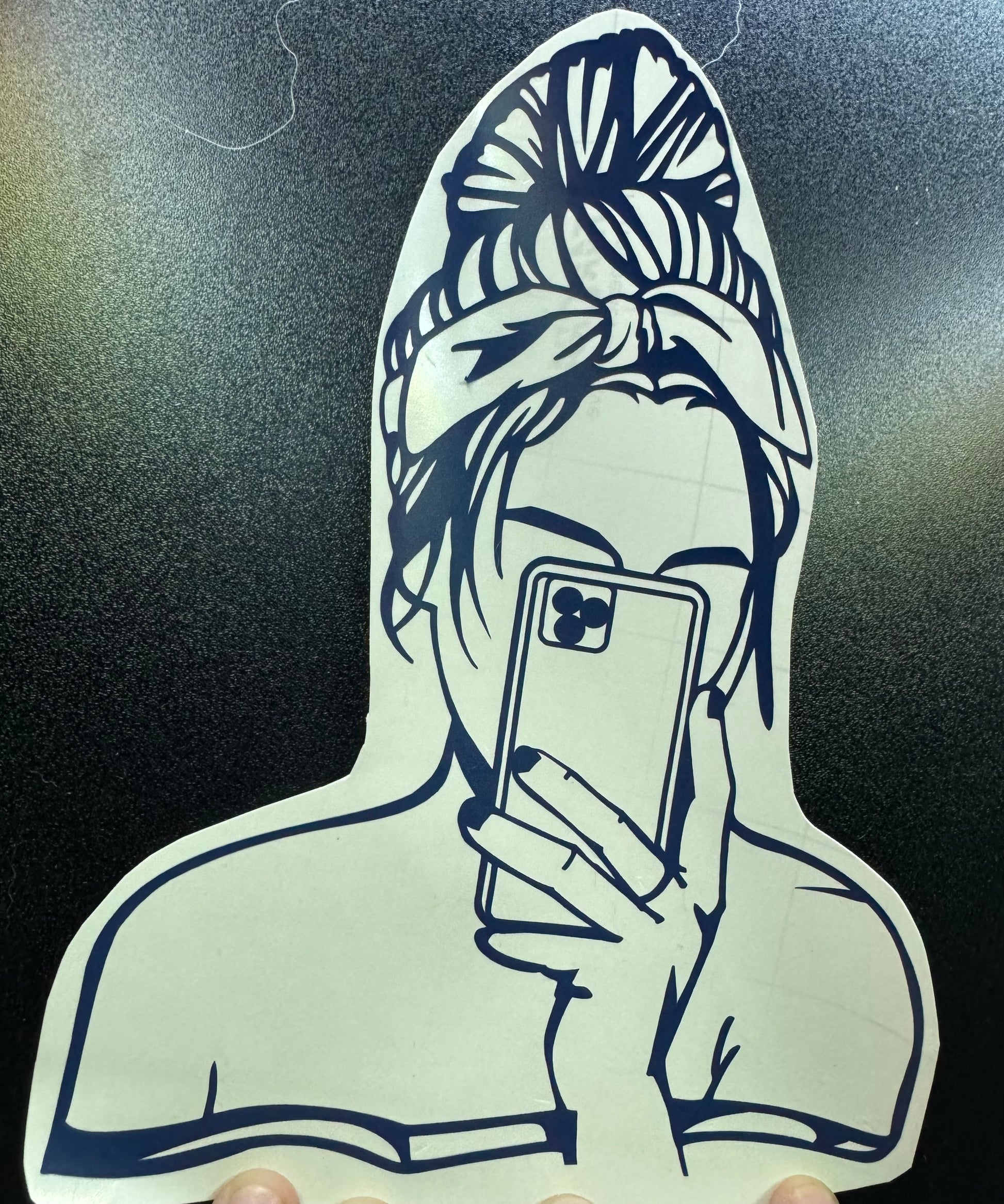 A black and white decorative decal with a design of a person wearing a hoodie with a patterned hood, holding a smartphone.
